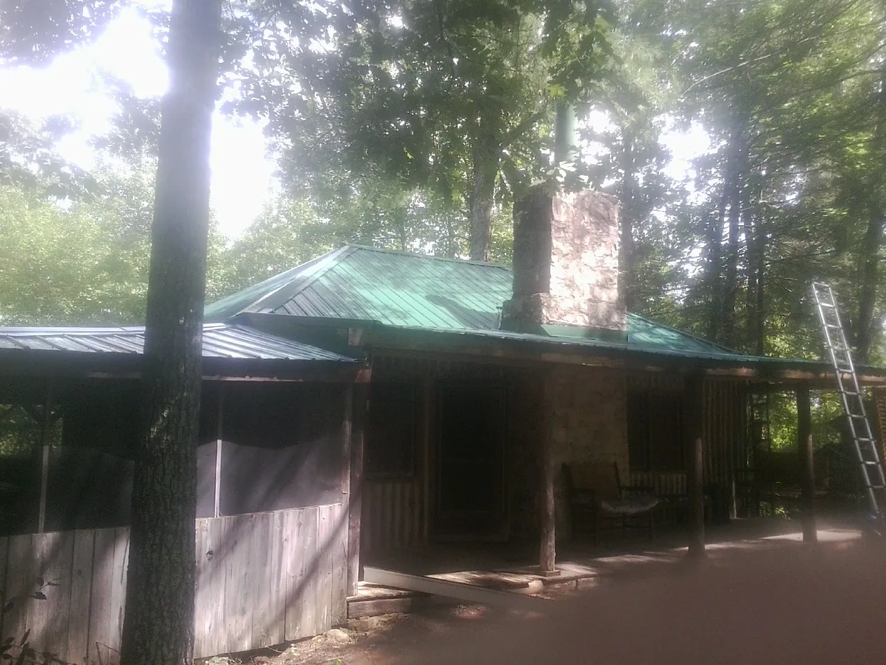 Green metal roof and stone chimney above a log cabin porch in Nichols