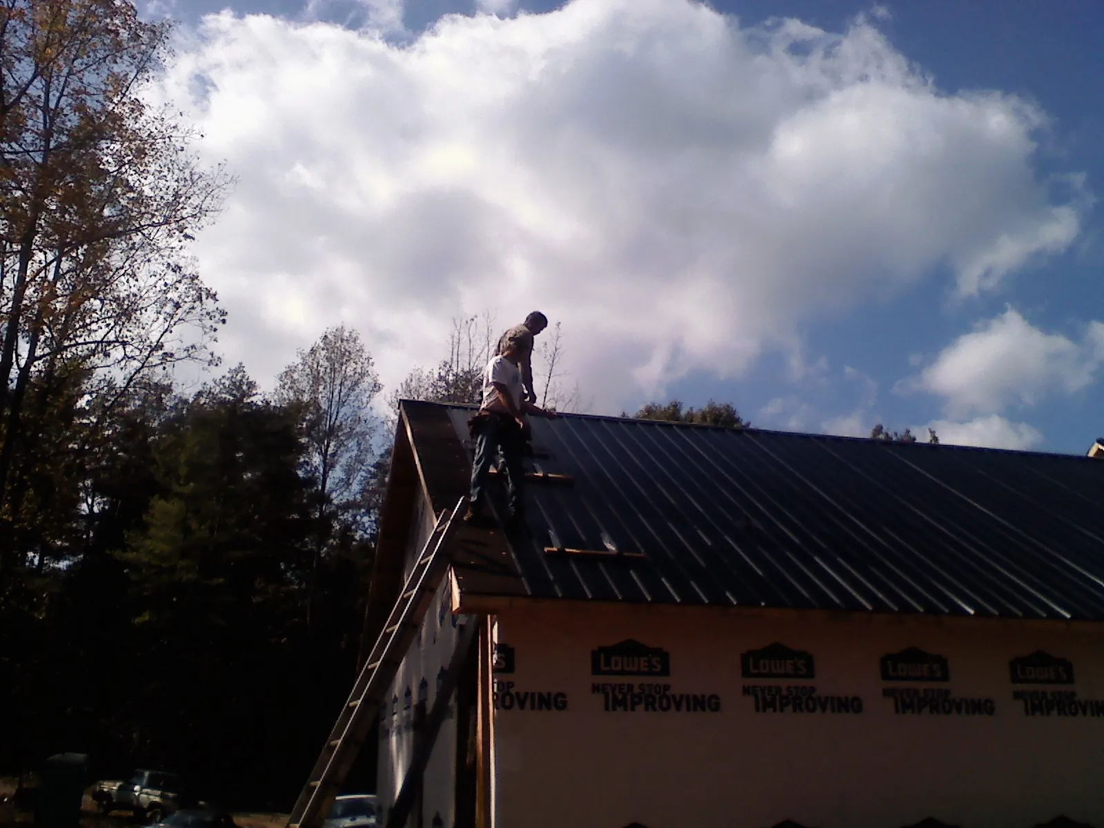 Roofer fastening dark metal panels high against a cloudy sky, from a Roof Inspection job in Nichols